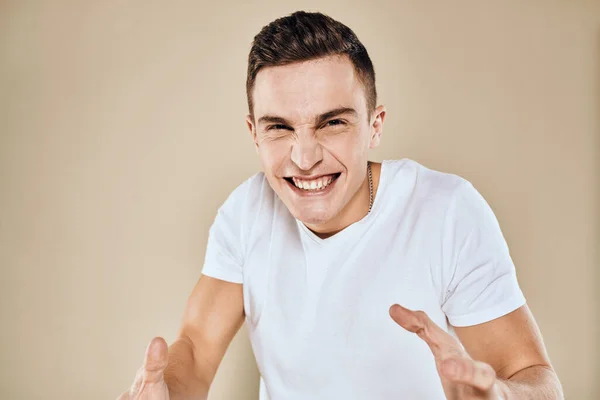Uomo con espressione facciale scontenta emozioni bianco gesti t-shirt con le mani sfondo beige — Foto Stock