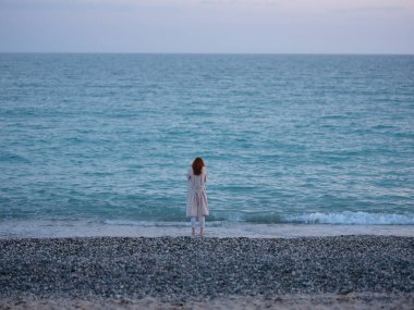 Okyanusun kıyısında beyaz pantolonlu bir kadın.