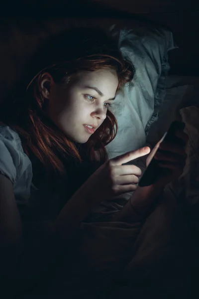 woman lying in bed with phone in hand watching news before bedtime