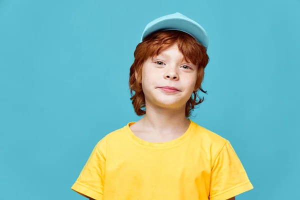 cute redhead boy looking ahead yellow tshirt blue cap cropped view