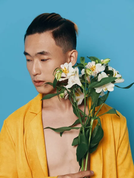 Homem romântico com um buquê de flores em um fundo azul e um casaco amarelo, aparência asiática — Fotografia de Stock