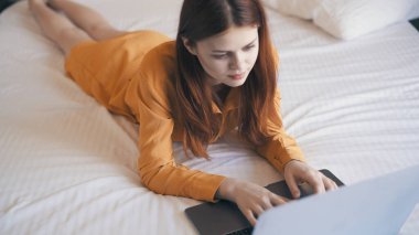 Kadın evde dizüstü bilgisayarın önünde yatıp daktilo çalışıyor.