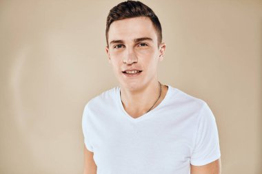 Sevimli duygusal adam beyaz tişört jesti elleri kırpılmış bej renkli stüdyo arka planı