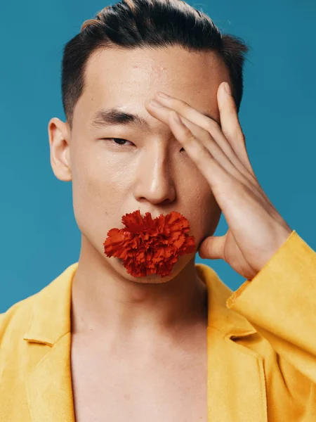 アジア系の男が手で顔に触れ、口の中に赤い花を咲かせている。クローズアップ肖像画 — ストック写真