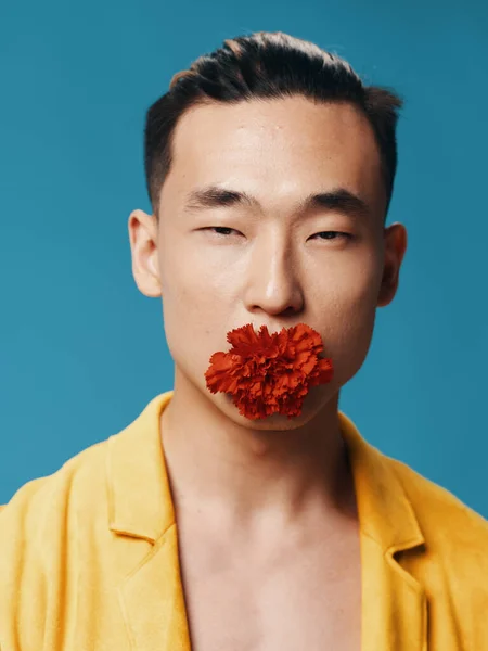 口の中に細い目の黄色いジャケットと赤い花を持つ韓国の男性 — ストック写真