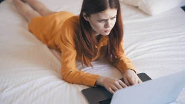 Kadın evde dizüstü bilgisayarın önünde yatıp daktilo çalışıyor.