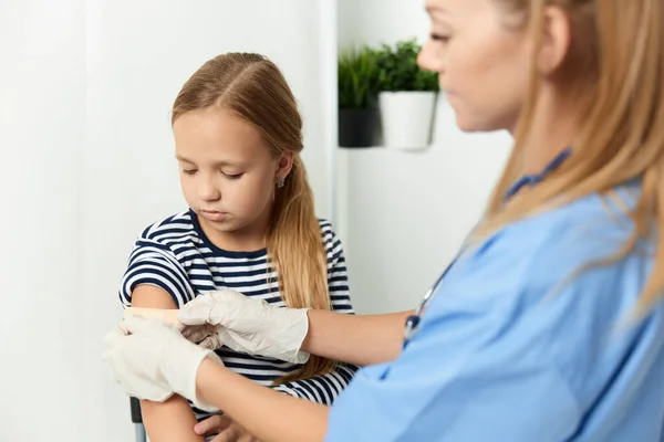 Uma mulher médico ao lado de uma menina sela a mão com um adesivo de saúde — Fotografia de Stock