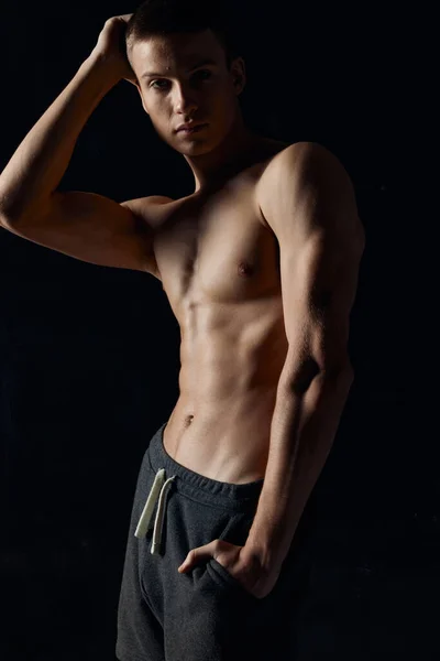 Sportoló testépítő kezével közel az archoz és szürke nadrágban fekete háttér — Stock Fotó