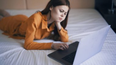 Kadın yatak odasında dizüstü bilgisayarın önünde yatıyor ve evde çalışıyor.