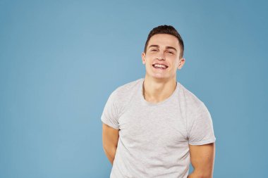 Beyaz tişörtlü neşeli bir adam elleri ve duyguları mavi arka planda hareket ediyor.