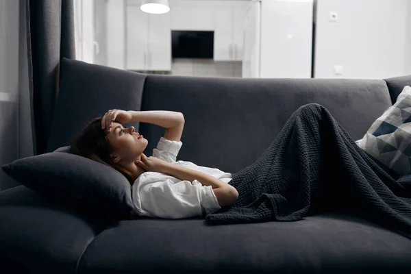 Una mujer en una habitación cómoda se encuentra en un sofá cubierto con una manta gris —  Fotos de Stock