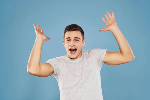 Vrolijk man in een wit t-shirt gebaren met zijn handen emoties blauw achtergrond — Stockfoto