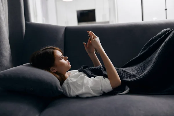 Mujer descansando acostada en el sofá con el teléfono móvil en la mano recortado vista —  Fotos de Stock