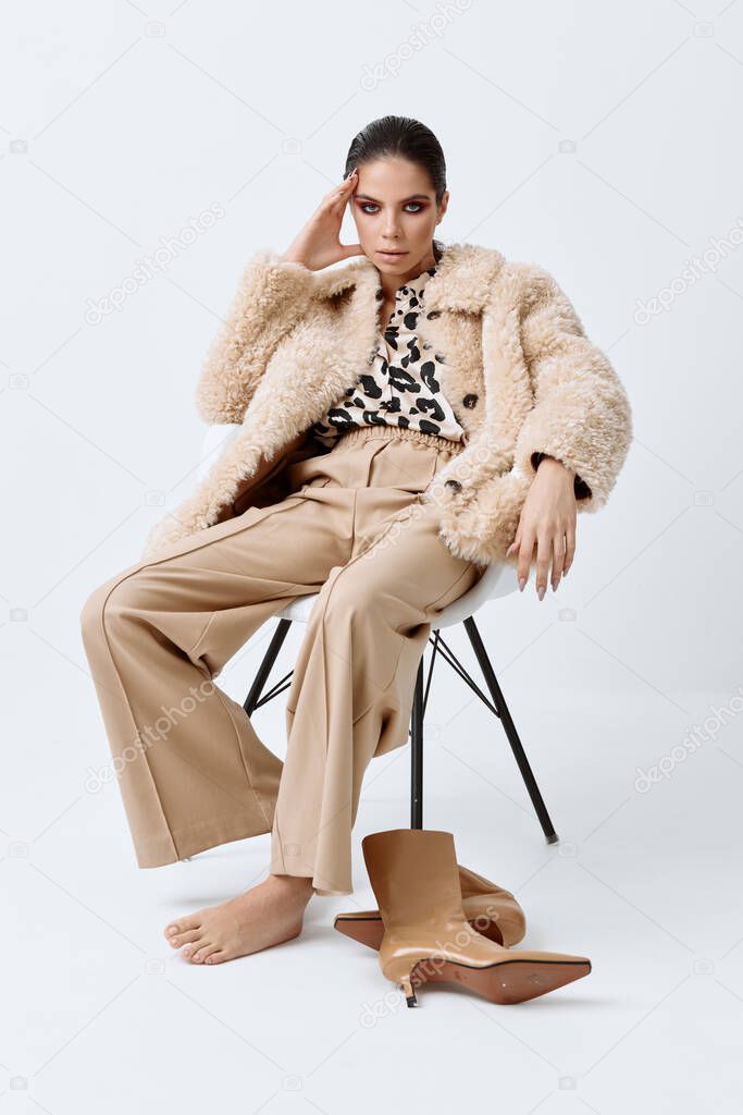 pretty brunette in luxurious clothes sitting on a chair light background
