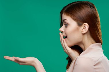 Şaşırmış bir kadın, duygularının önünde avuç içlerini tutarak yeşil arka planı yakından görüyor.