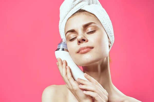 Ładna kobieta z ręcznikiem na głowie masażer w dłoniach kosmetologia czysta skóra różowe tło — Zdjęcie stockowe