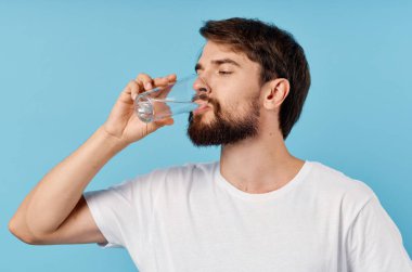 Güzel bir adam mavi arka plandaki bir bardaktan su içiyor. Yakın plan portresi.