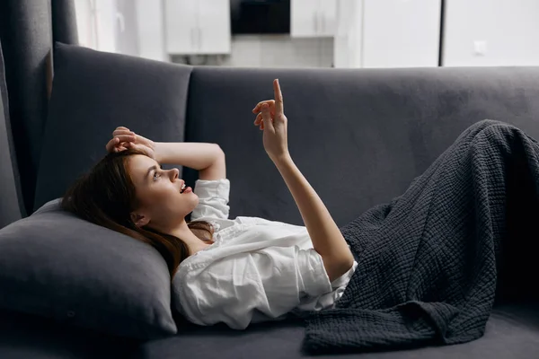 Uma jovem mulher em uma camiseta branca está deitada em um sofá dentro de casa vista lateral — Fotografia de Stock