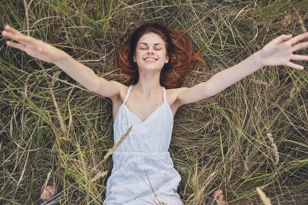 Mujer feliz se encuentra en la hierba seca y gestos con sus manos vestido blanco Copiar espacio —  Fotos de Stock