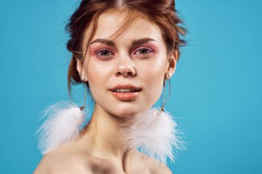 Çekici, çıplak omuzlar tüylü küpeler parlak makyaj mücevherleri mavi arka plan.