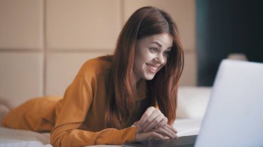 Yatak odasındaki duygusal kadın dizüstü bilgisayarın önünde uzanıyor.