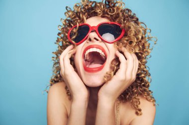 Kadın kırmızı dudaklı, ağzı açık, elleriyle yüzüne bakıyor. 