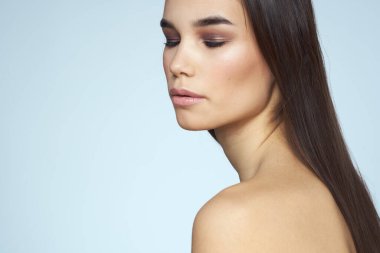 Güzel esmer, çıplak omuzlu, uzun saçlı, mavi arka planlı.