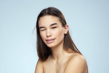 Güzel esmer, çıplak omuzlu, uzun saçlı, mavi arka planlı.