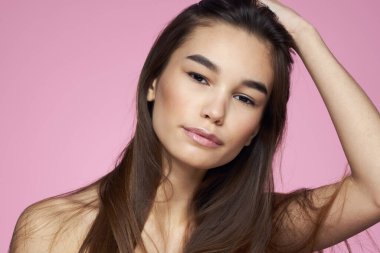 Güzel esmer, çıplak omuzlar, açık pembe arka plan.