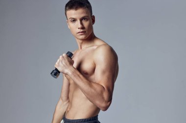 Ellerinde dambıllar olan atletik adam kollarının kasları üzerinde egzersiz yapıyor.