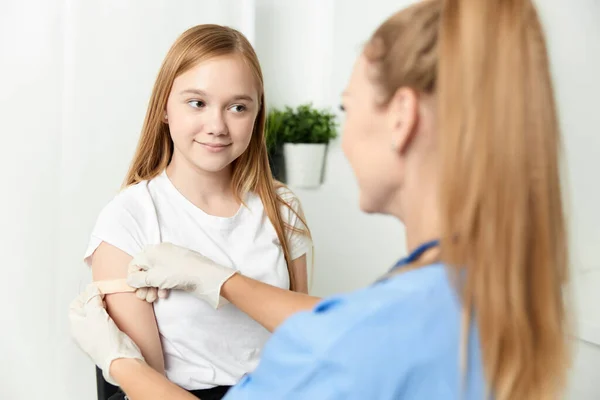 En kvinnlig läkare bredvid en flicka förseglar armen med en gipsvaccination — Stockfoto