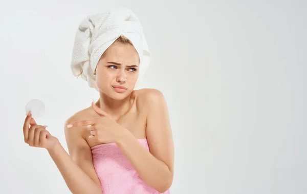 Donna in asciugamani rosa utilizzando la cura della pelle del viso in mano sfondo grigio — Foto Stock