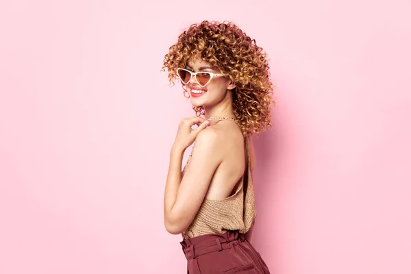 Mujer atractiva pelo rizado sonrisa gafas de sol rosa fondo ropa de moda — Foto de Stock