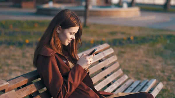 Mujer en el parque sentada en un banco con un teléfono en las manos — Foto de Stock