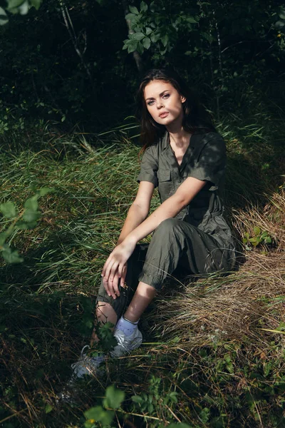 Mujer en overoles verdes y zapatillas de deporte en hierba seca en el borde del bosque —  Fotos de Stock
