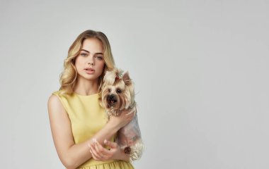 Sarı elbiseli bir kadın kucağında küçük bir köpek tutuyor.