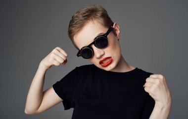 Kısa saçlı ve koyu gözlükle makyaj yapan kırmızı dudaklı bir kadın.