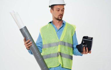 Sarı yelek giyen bir adam ve elinde bir rulo kağıt olan beyaz bir miğfer işi hallediyor.