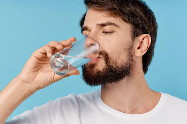 Hermoso hombre beber agua de un vaso sobre un fondo azul primer plano retrato — Foto de Stock