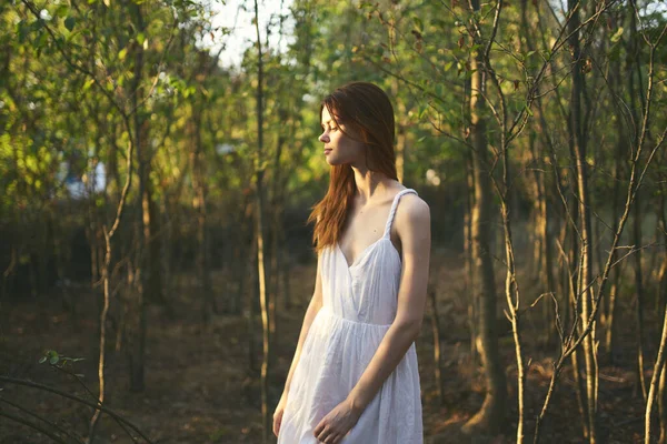 Bahçedeki ağaçların yanında bir kadın yaz tatili için beyaz elbise giyiyor. — Stok fotoğraf