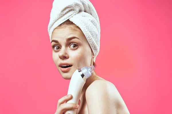 Fröhliche nationale Frau mit einem Handtuch auf dem Kopf Massagegeräte in den Händen Hautpflege Wellness-Behandlungen rosa Hintergrund — Stockfoto
