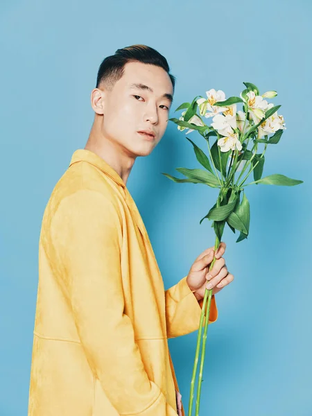 Vista lateral de um cara com um buquê de flores em um casaco amarelo em um fundo azul — Fotografia de Stock