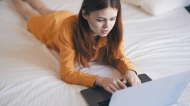 Kadın evde dizüstü bilgisayarın önünde yatıp daktilo çalışıyor.