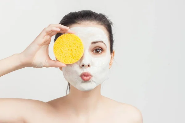 Wanita dengan bahu telanjang krim masker di wajah menggosok spons — Stok Foto