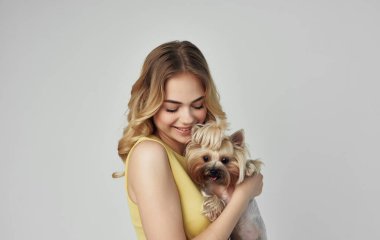 Sarı elbiseli neşeli bir sarışın elinde safkan bir köpek tutuyor.