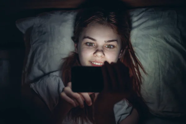woman holding phone in her hands lying in bed at night lifestyle