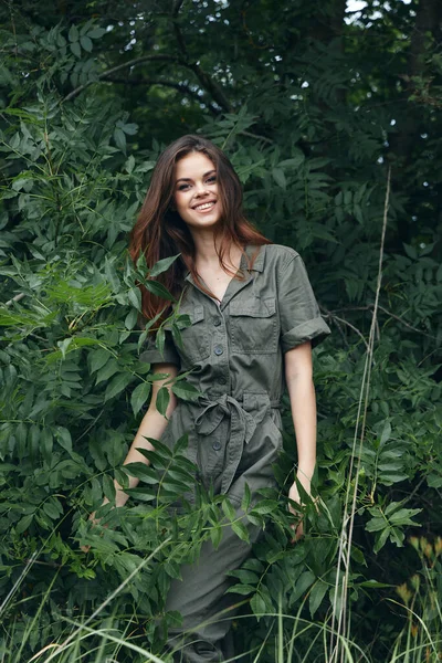 Woman in the forest near the green bushes a dazzling smile and a green jumpsuit green leaves