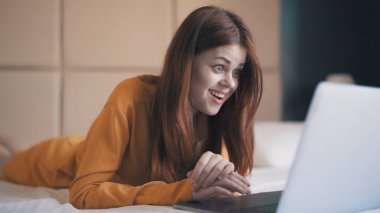 Yatak odasındaki duygusal kadın dizüstü bilgisayarın önünde uzanıyor.