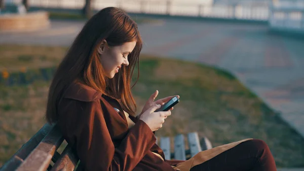 Mujer en el parque sentada al aire libre con un teléfono en las manos vista lateral — Foto de Stock