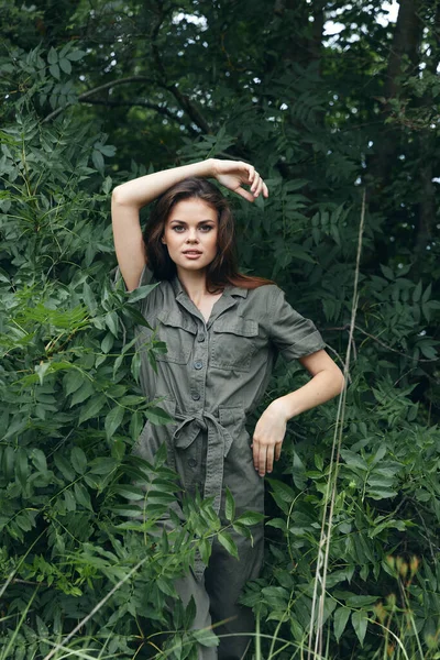 Woman in the forest In overalls near the bushes, holds his hand above his head trees